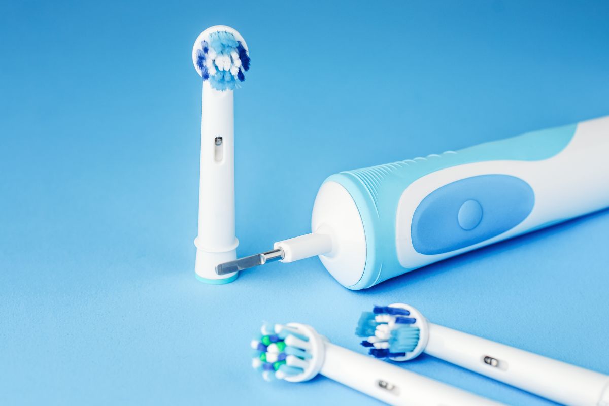 Spazzolino elettrico con testine intercambiabili su sfondo azzurro: strumento consigliato per la pulizia delicata degli impianti dentali fissi.
