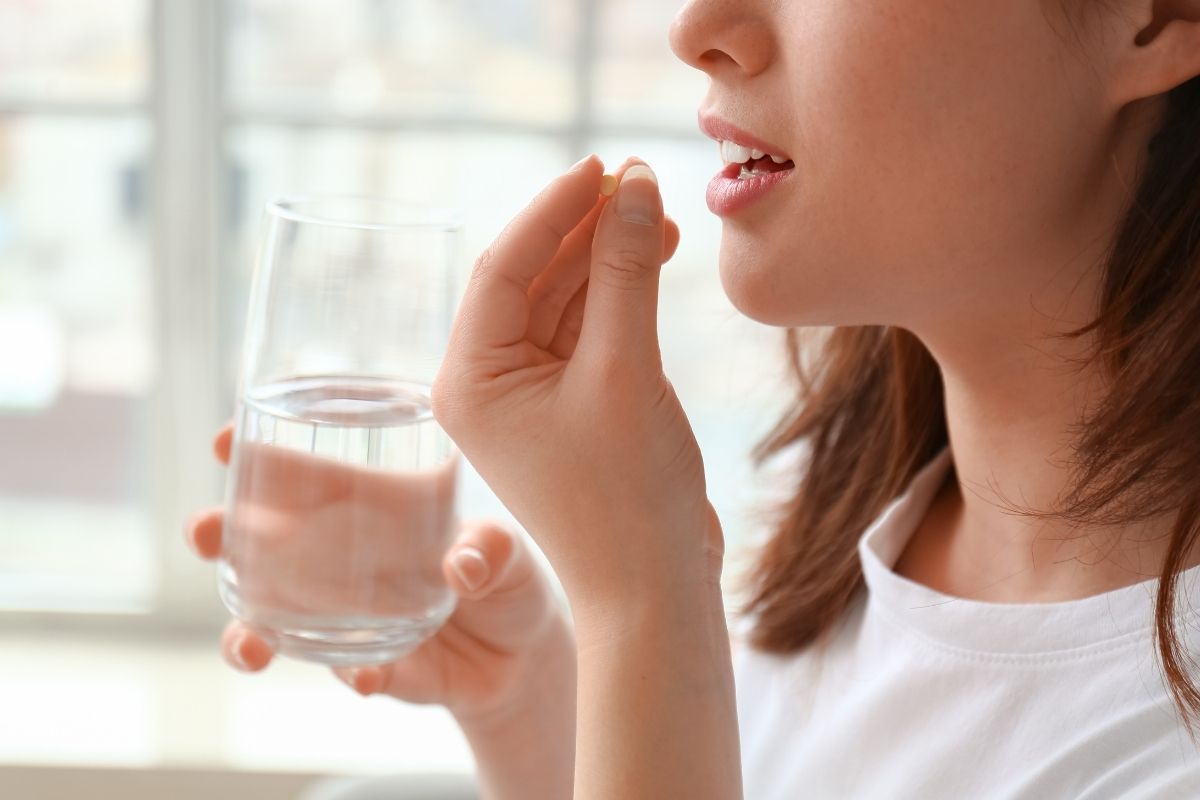 Primo piano di una paziente che assume una compressa di antinfiammatorio con un bicchiere d'acqua, a simboleggiare l'importanza di seguire la terapia prescritta dopo aver messo un impianto dentale