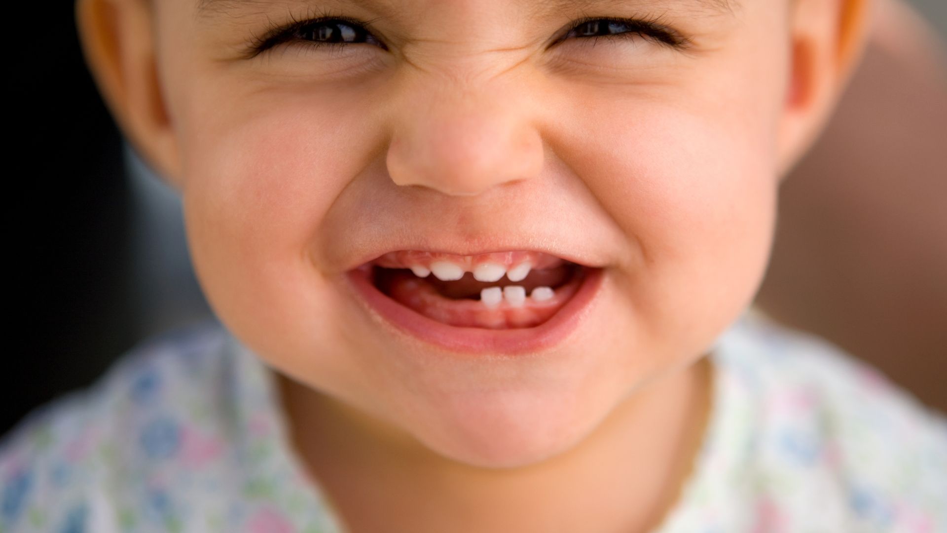 Dettaglio sulla bocca di un bambino che fa un grande sorriso, mettendo in mostra i denti da latte sani e sottolineando l'importanza dell'igiene orale fin dalla prima età